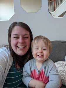 A woman sits on the couch, smiling with her toddler.