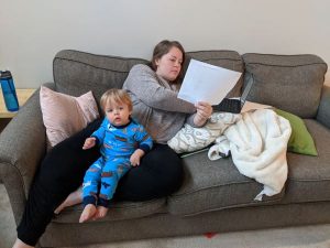 A woman is working on a couch while a toddler sits on her lap.