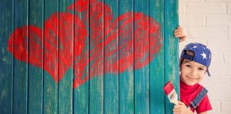 kid paints red hearts on turquoise wall