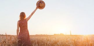woman waving goodbye with a hat in a field at sunset
