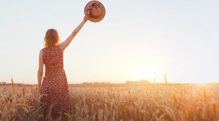 woman waving goodbye with a hat in a field at sunset
