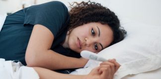 woman lying in bed, looking at a pregnancy test