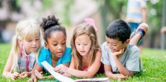 four young kids reading a book together