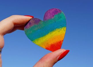 rainbow heart being held between thumb and pointer finger