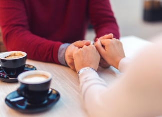 couple holding hands next to two cups of coffee