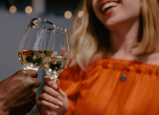 Blurred shot of woman in orange shirt clinking her glass of white wine with another person's glass of white wine.