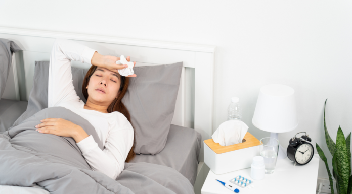 Asian woman laying in bed with hand to forehead, holding facial tissue.