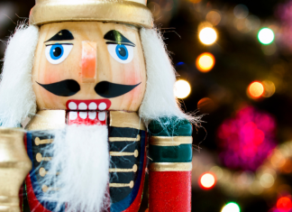Image of a nutcracker standing in front of a blurred lighted Christmas tree background
