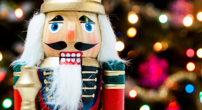 Image of a nutcracker standing in front of a blurred lighted Christmas tree background