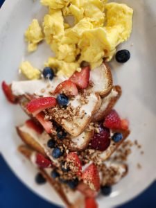 Plated gourmet French toast with fruit topping and side of scrambled eggs