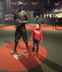 Small child in KC Chiefs hoodie looking at statute of baseball player.